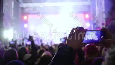 手里拿着智能手机的歌迷们在生动的舞台灯光下欣赏现场音乐